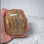Polished peach-brown crystal stone held in hand, rounded form and glossy sheen
