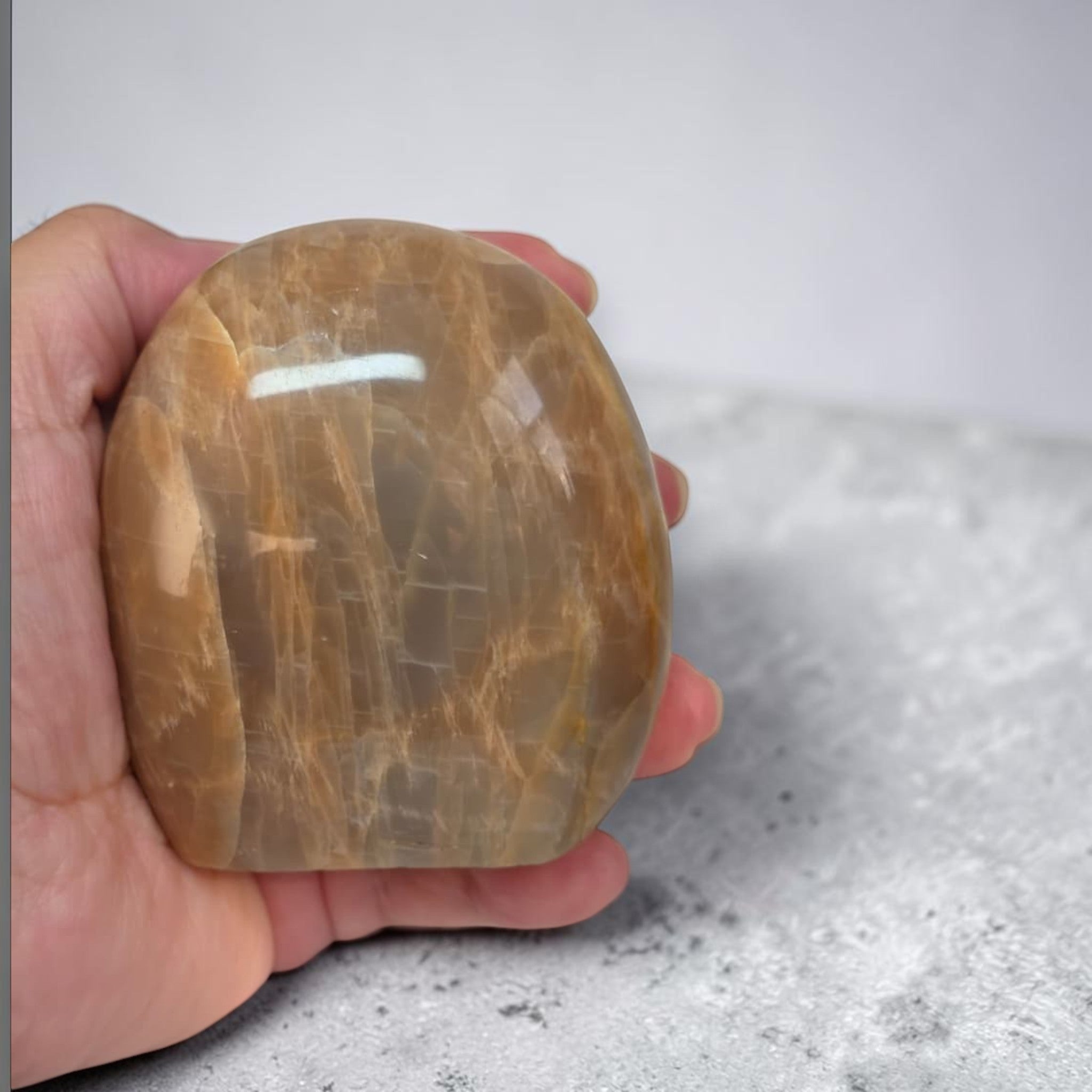 Polished peach-brown crystal stone held in hand, rounded form and glossy sheen