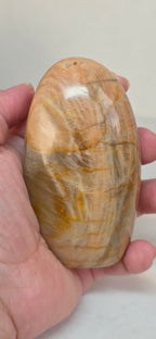 Polished peach moonstone freeform crystal, held in hand, smooth oval.