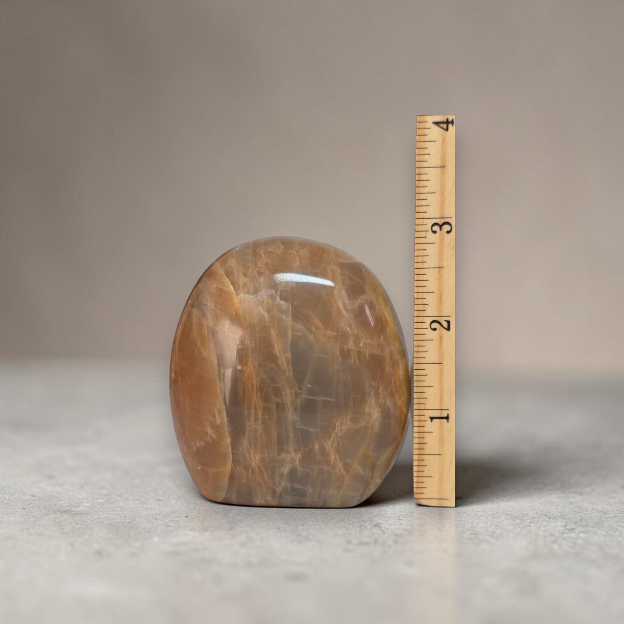 Polished peach-brown freeform crystal next to measuring ruler, oval shape