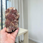 Pink amethyst crystal cluster slab with dark rock matrix, held in a hand
