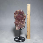 Pink amethyst crystal cluster slab on black circular metal stand, with measuring ruler