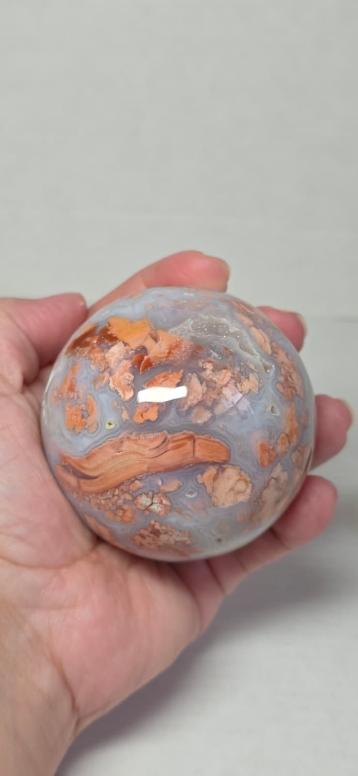Agate sphere held in hand, blue-gray with orange-brown streaks and pits