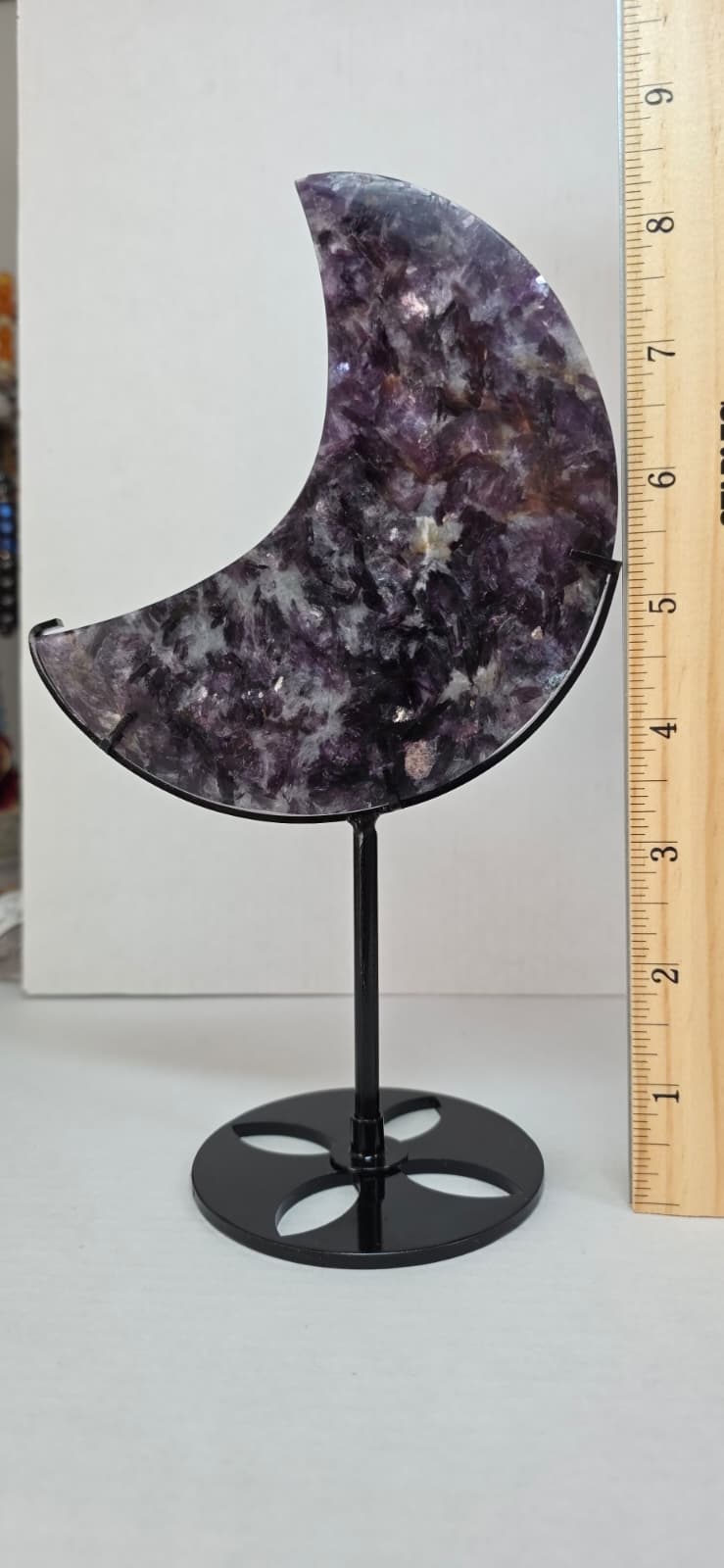 Purple speckled crescent moon crystal decor on black metal stand beside measuring ruler