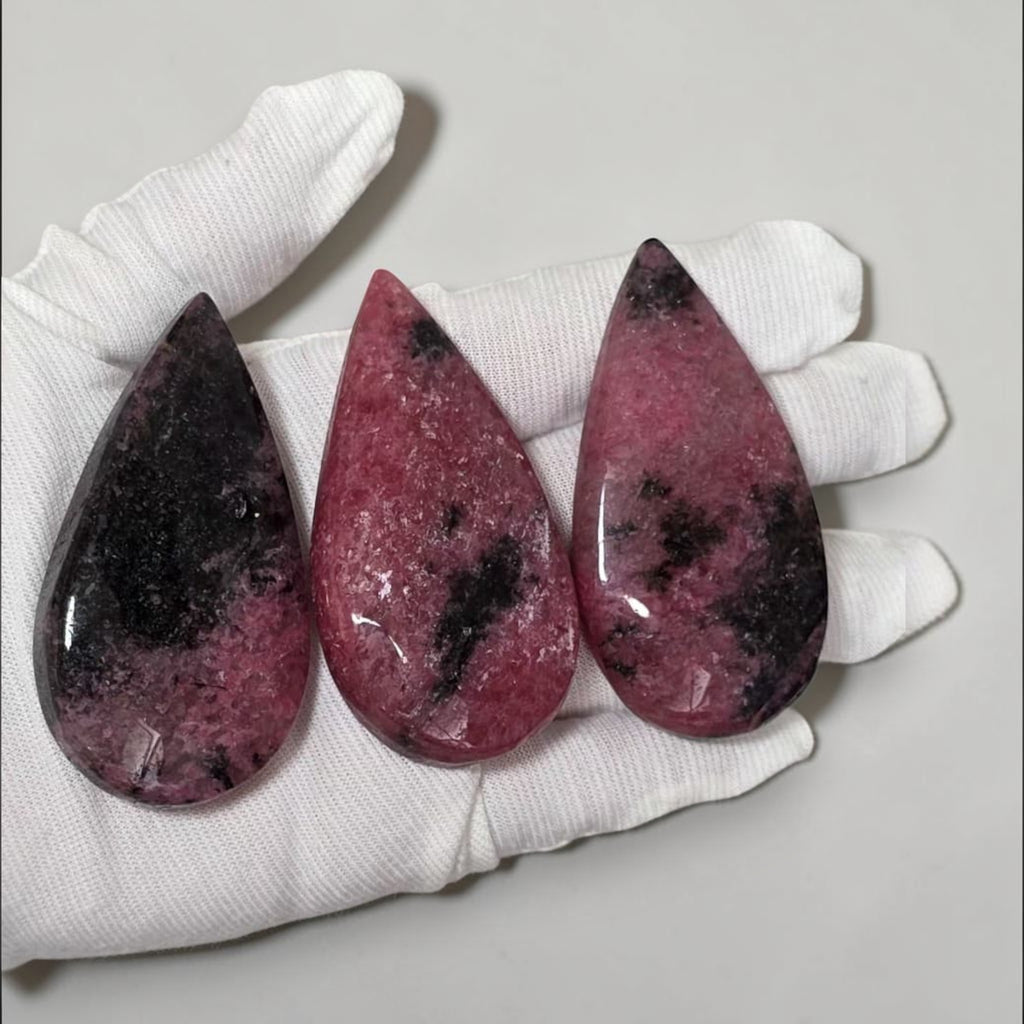 Rhodonite teardrop crystals in white gloves: three pink pieces with dark mottling and shine