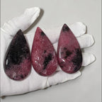 Rhodonite teardrop crystals in white gloves: three pink pieces with dark mottling and shine