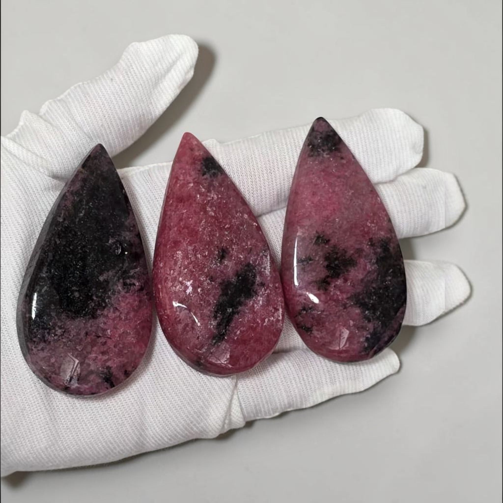 Rhodonite teardrop crystals in white gloves: three pink pieces with dark mottling and shine