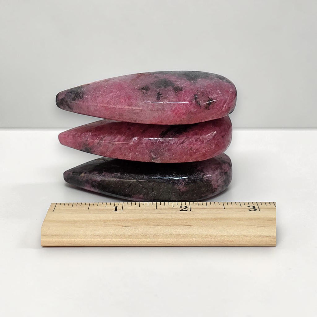 Rhodonite polished stone stack with ruler for scale; pink pieces with dark streaks