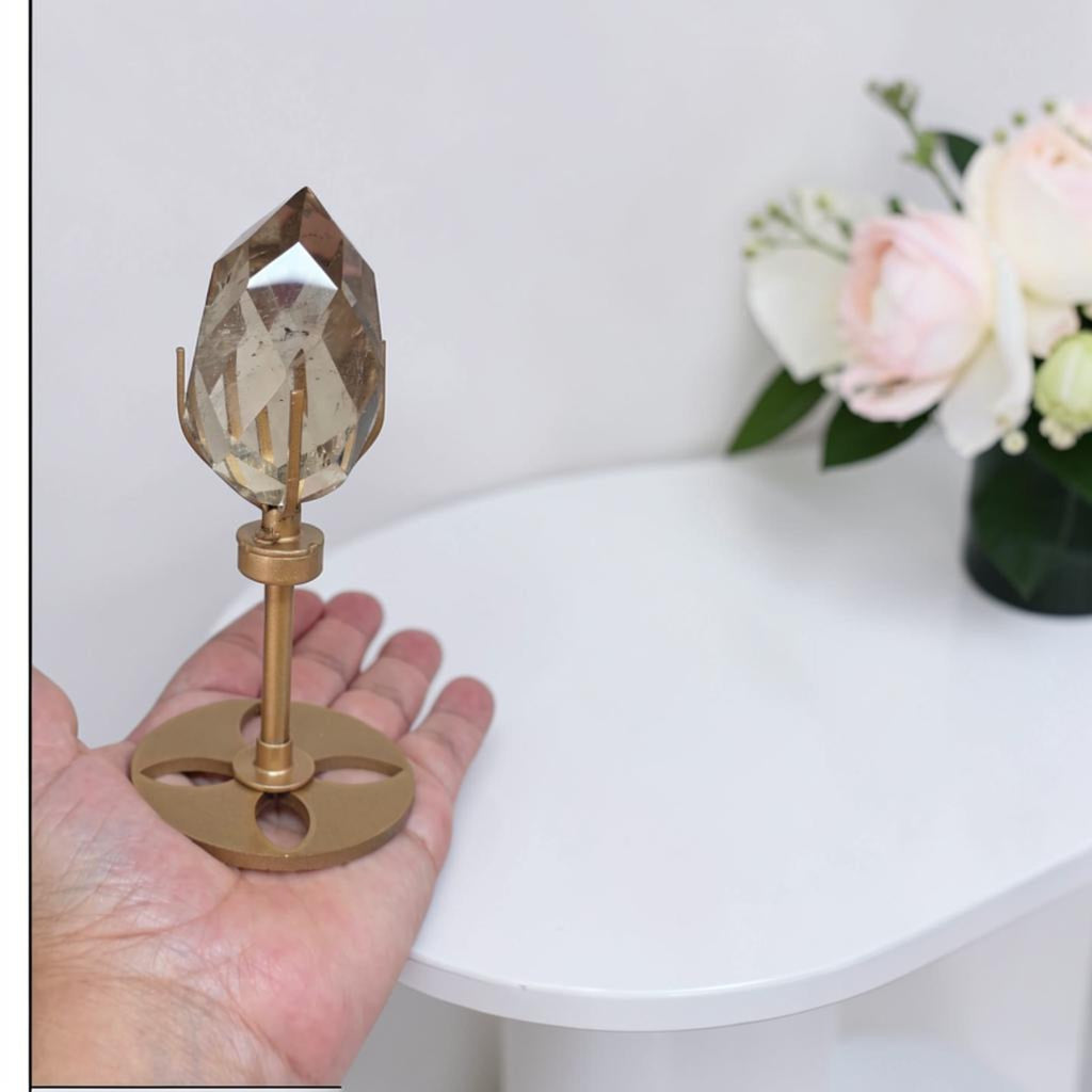 Smoky quartz faceted freeform on gold stand, held upright by a hand