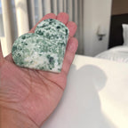 Heart-shaped green and white stone held in a hand with a blurred indoor background