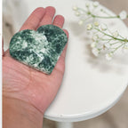 Heart-shaped green stone held in a hand with a blurred background