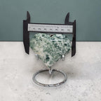 Heart-shaped green stone on a stand with a ruler for scale against a gray background