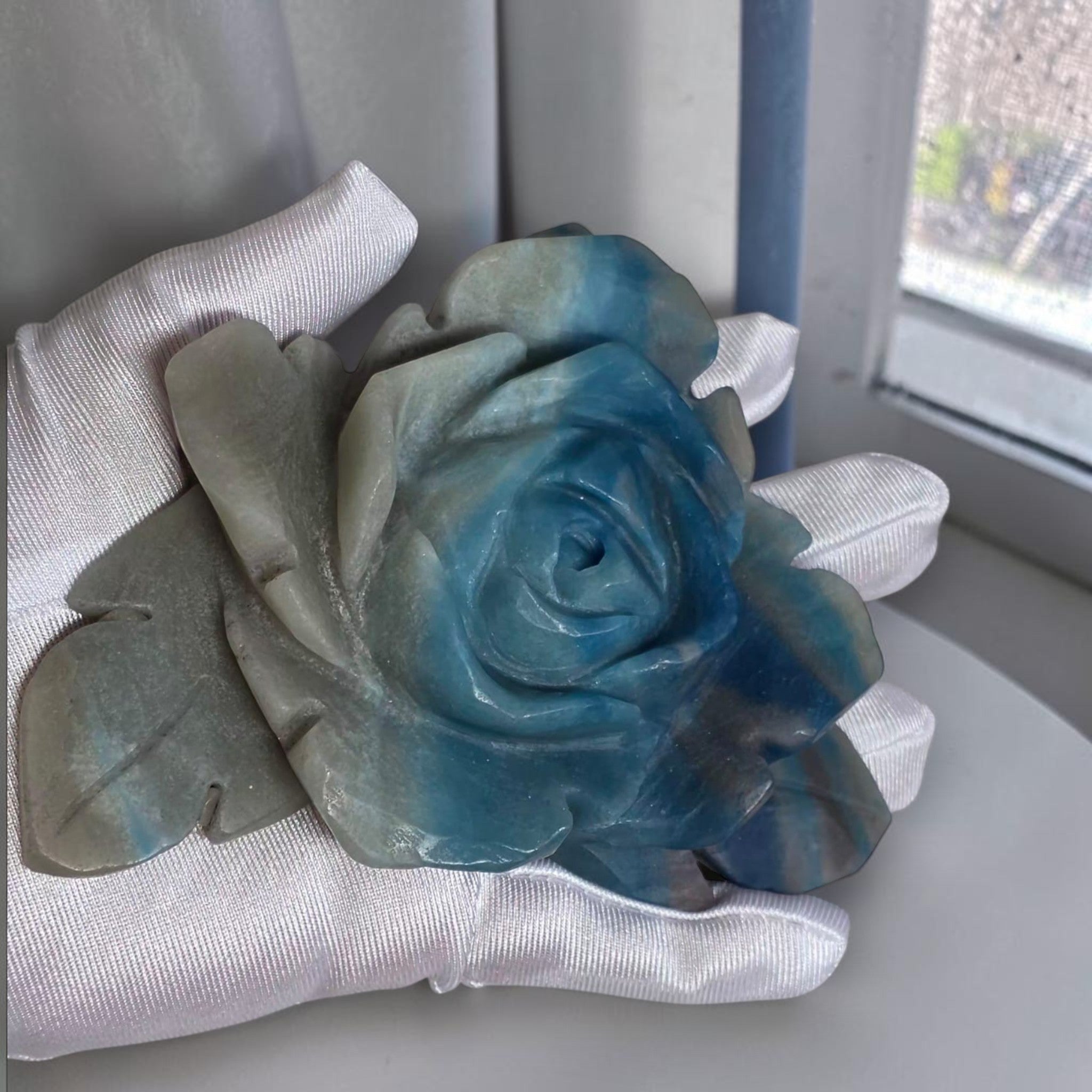 Natural Trolleite rose carving held in gloved hand showing size and blue-grey color detail