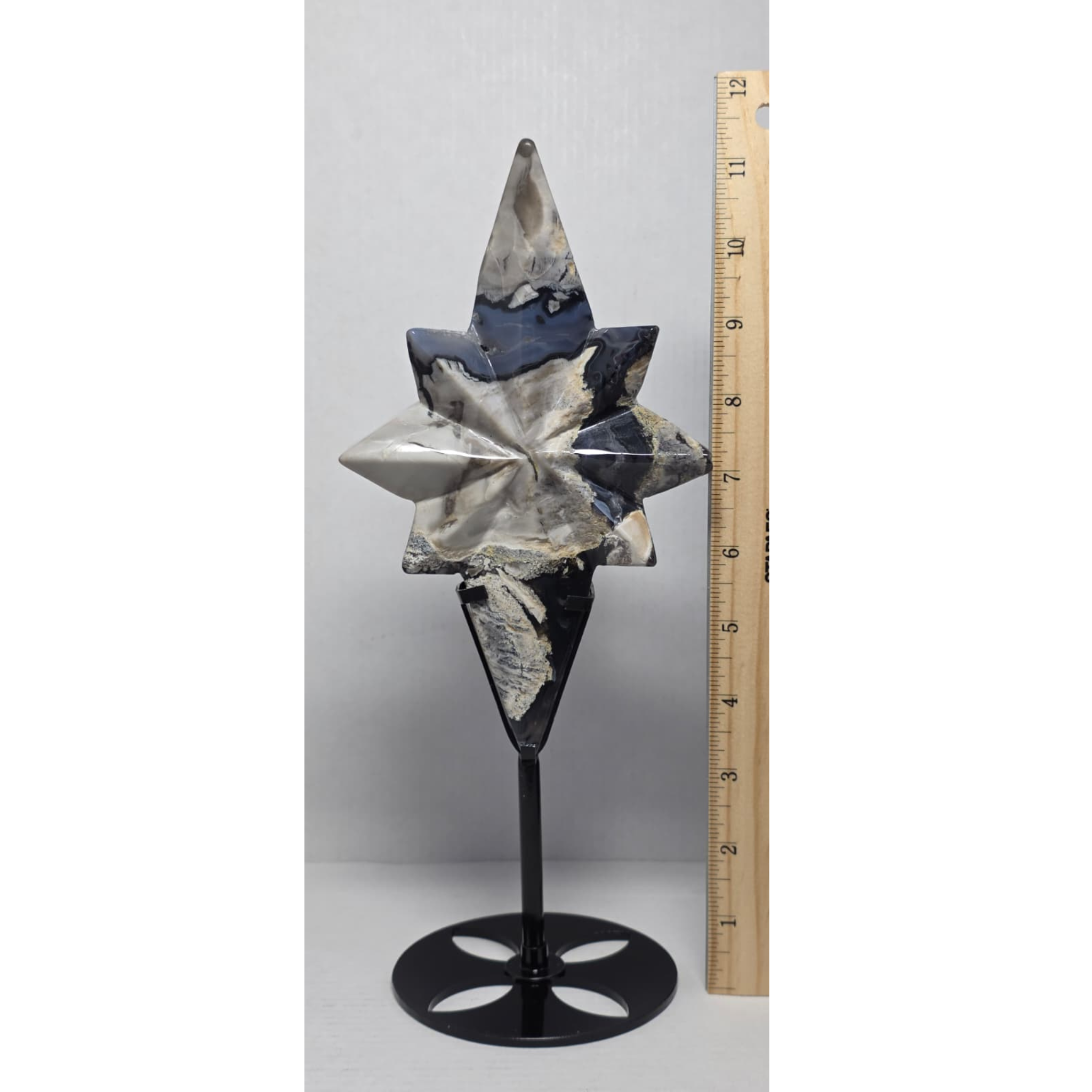 Star agate crystal carving on black stand with measuring tape beside it, gray and blue
