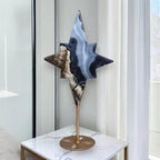 Faceted star crystal sculpture with dark and blue tones on a gold stand with round base.