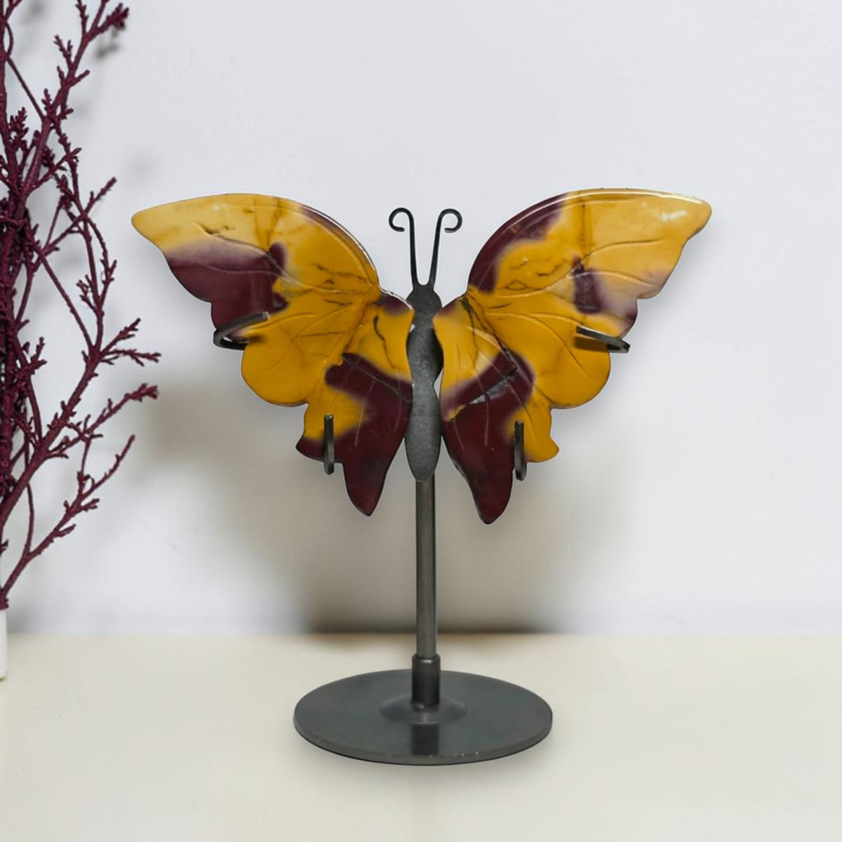 Small yellow and burgundy Mookaite Jasper butterfly on a dark metal stand